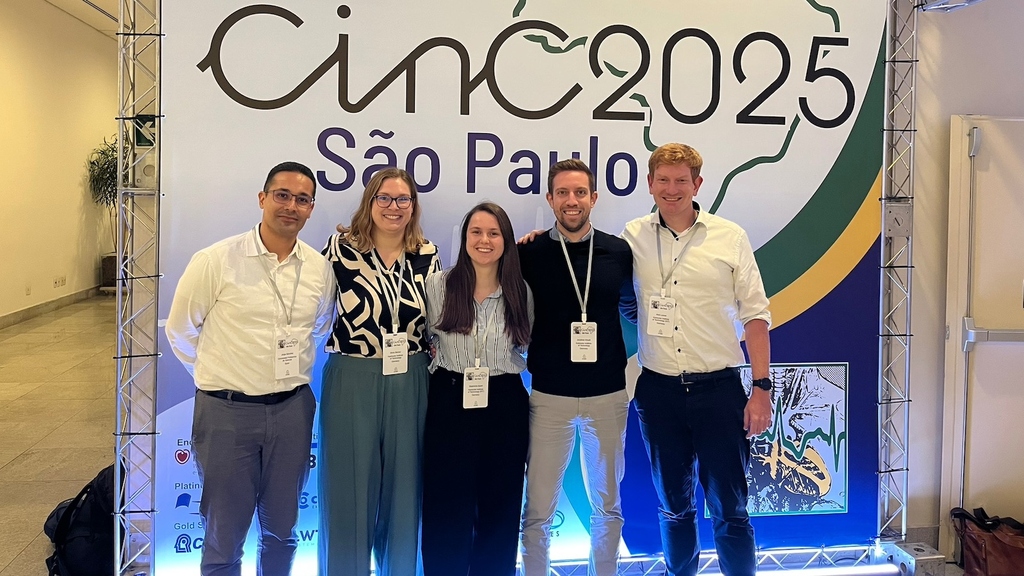 Fünf Teilnehmende posieren vor einem Banner der cinC 2025 Konferenz in São Paulo.